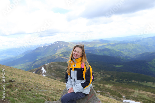 Young happy female tourist wearing yellow jacket sitting in Carpathian mountains. photo