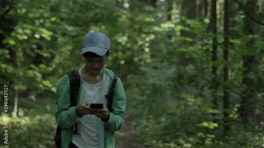 boy walking in the forest and uses a phone outdoors boy walking in the forest and uses a phone outdoors