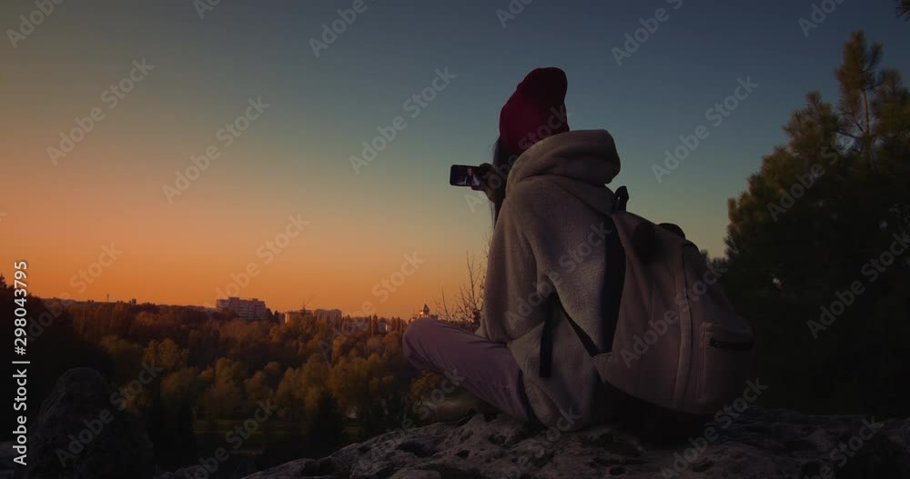 Young female sitting on a cliff at sunset doing a selfie. Young female sitting on a cliff at sunset doing a selfie.