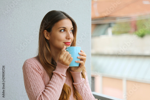 Portrait of beautiful girl with warm sweater enjoying hot drink in the morning at home before going to work outdoors.