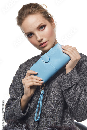 Fotografija Medium close-up shot of a young brown-haired European lady in a gray mottled jacket with a textured blue leather wallet with a buckle opening closure and a wristlet strap handle in her hands