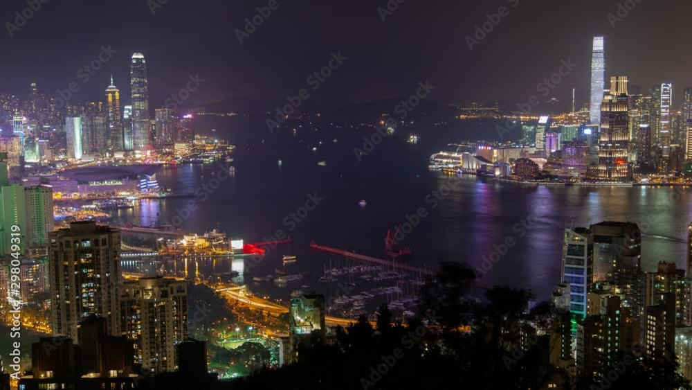 Timelapse Hong Kong city highrise buildings surround harbour with sailing boats and city reflection on dark water against hill silhouettes at night zoom out Timelapse Hong Kong city highrise buildings surround harbour with sailing boats and city reflection on dark water against hill silhouettes at night zoom out