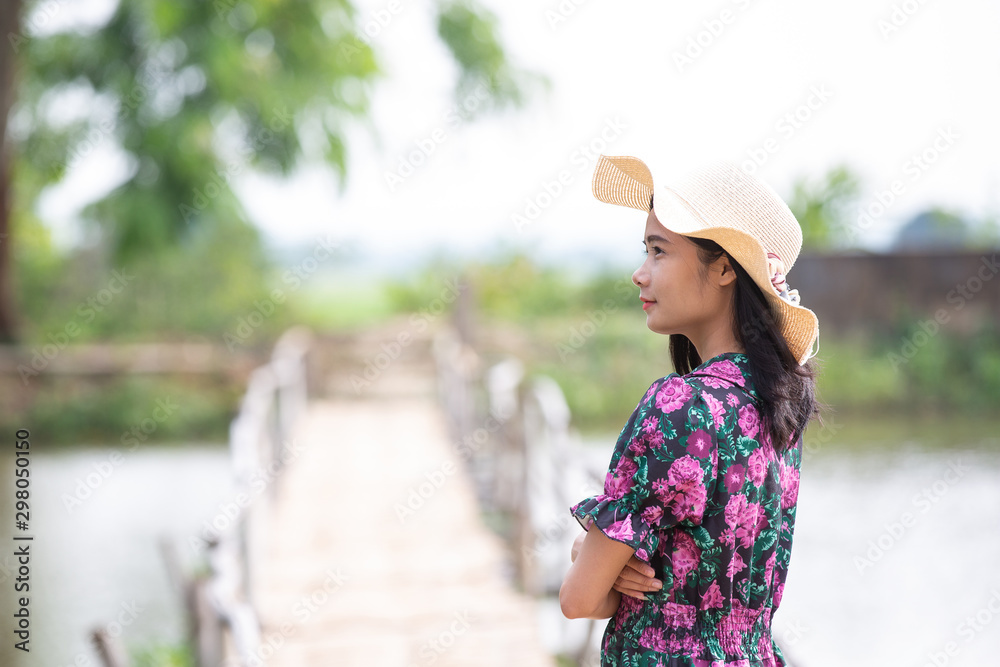 The girl wearing a red floral dress and a hat was standing in front of the pan on the side.
