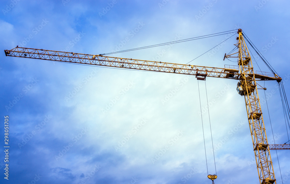 yellow construction crane against blue clouds cloudy sky. Place under the text copy space