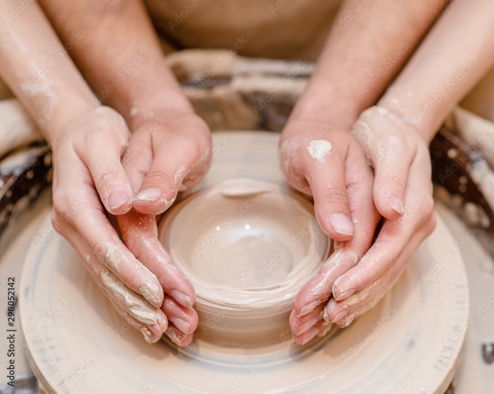 loving couple in the studio make clay dishes together on a potter’s wheel