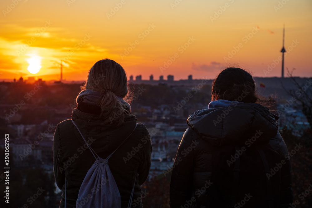 Two friends looking at the sunset over Vilnius, panorama with buildings and the TV tower