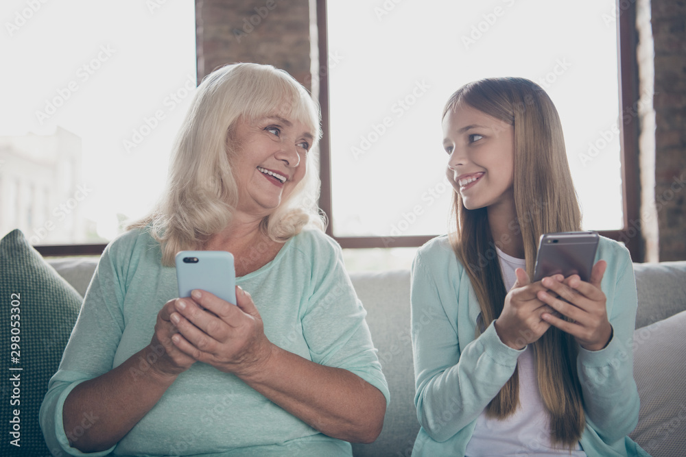 Photo of two people cute aged white haired granny small granddaughter sitting cozy couch holding telephones hands spending free time weekend together house indoors Photo of two people cute aged white haired granny small granddaughter sitting cozy couch holding telephones hands spending free time weekend together house indoors