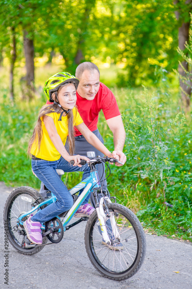 happy young father teaches his daughter to ride a bicycle in the summer park