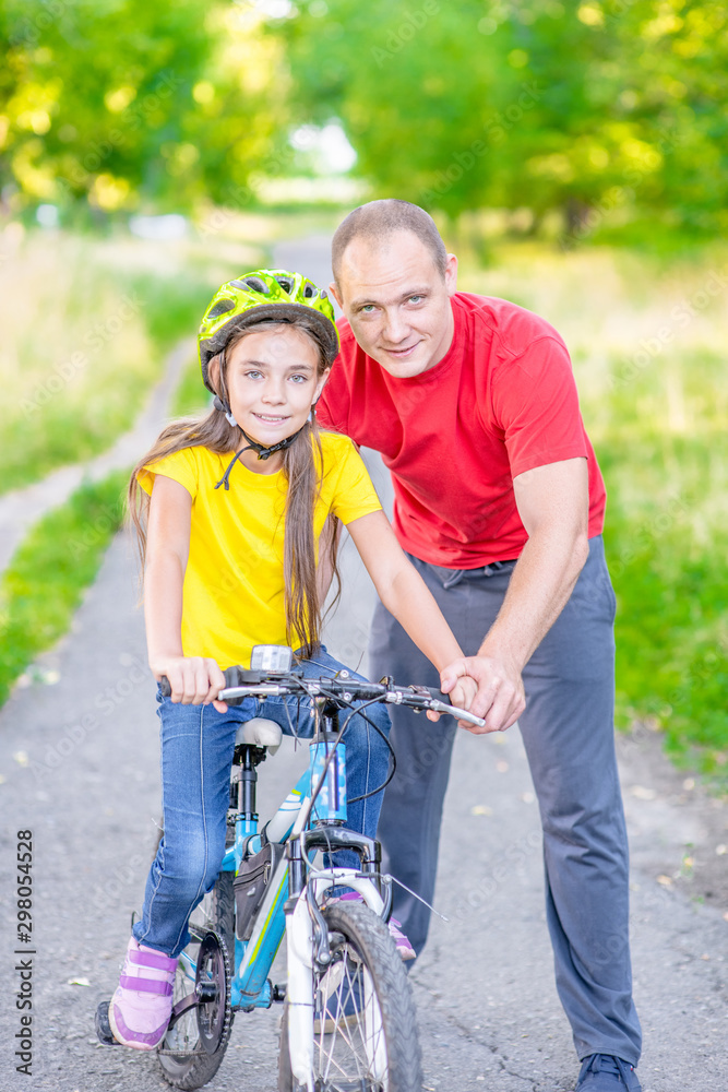 Happy family. A man helps his daughter learn to ride a bicycle in a summer park Happy family. A man helps his daughter learn to ride a bicycle in a summer park