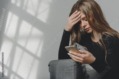 Portrait of a young sad crying girl with a smartphone in her hand.