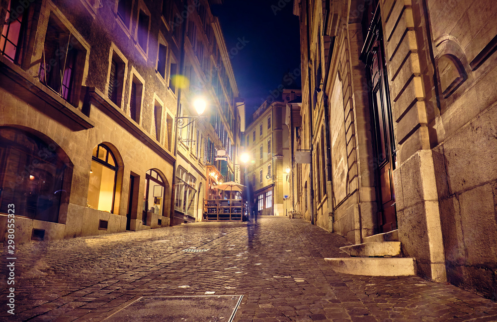 Street with old stone buildings in Geneva at night.