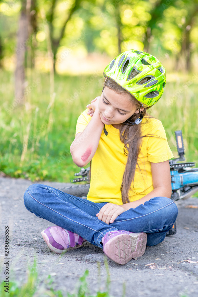 Sad little girl fell from the bike in the summer park