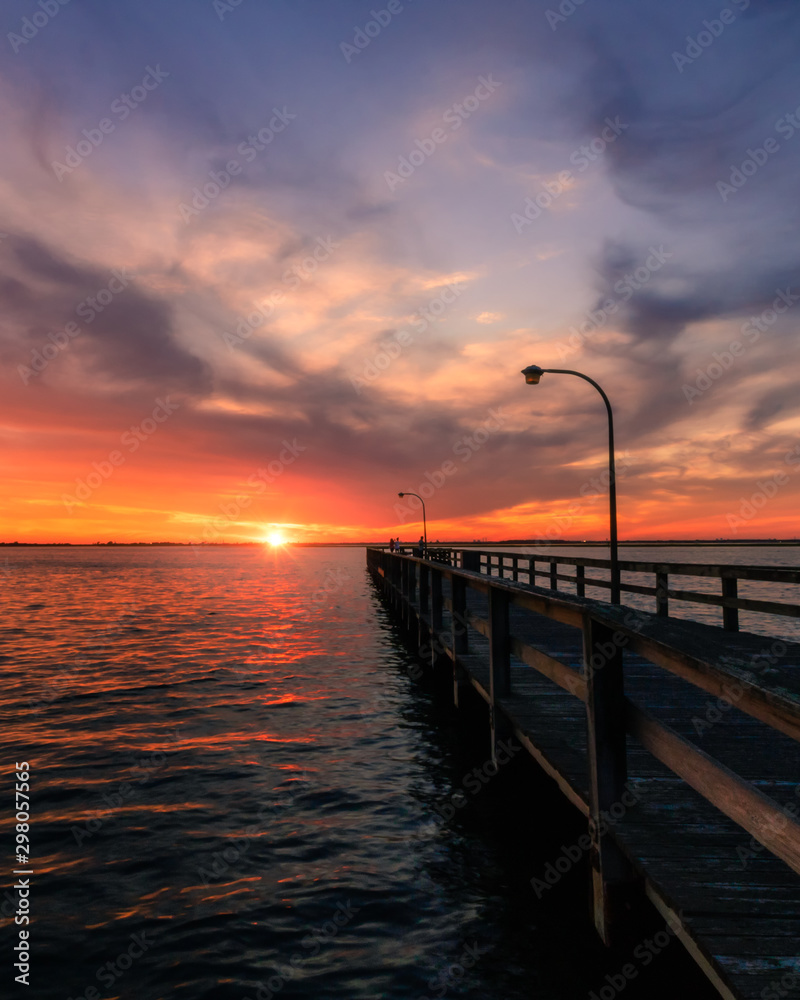 Beautiful vibrant colors in the sky over a long fishing pier as the sun dips below the horizon at sunset. 