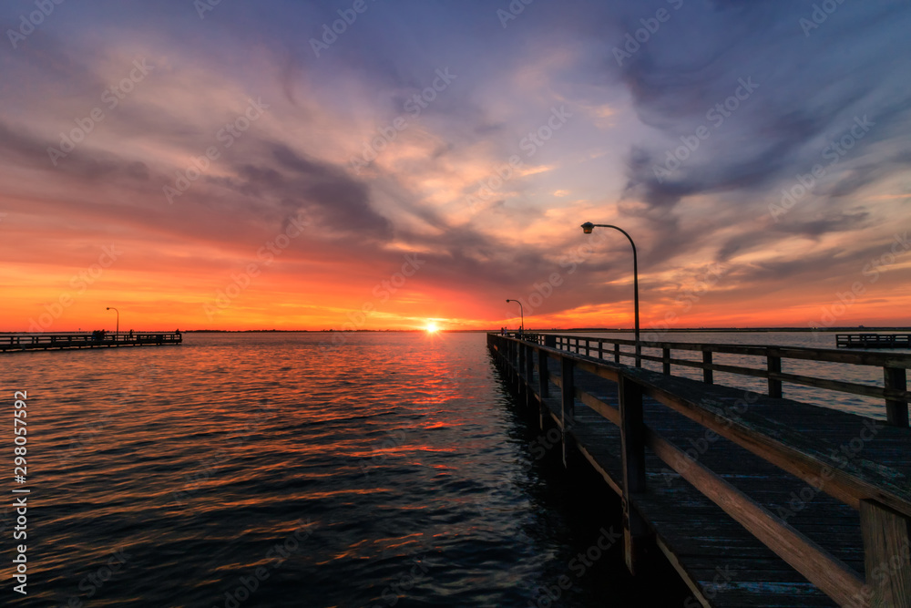 Beautiful vibrant colors in the sky over a long fishing pier as the sun dips below the horizon at sunset. 