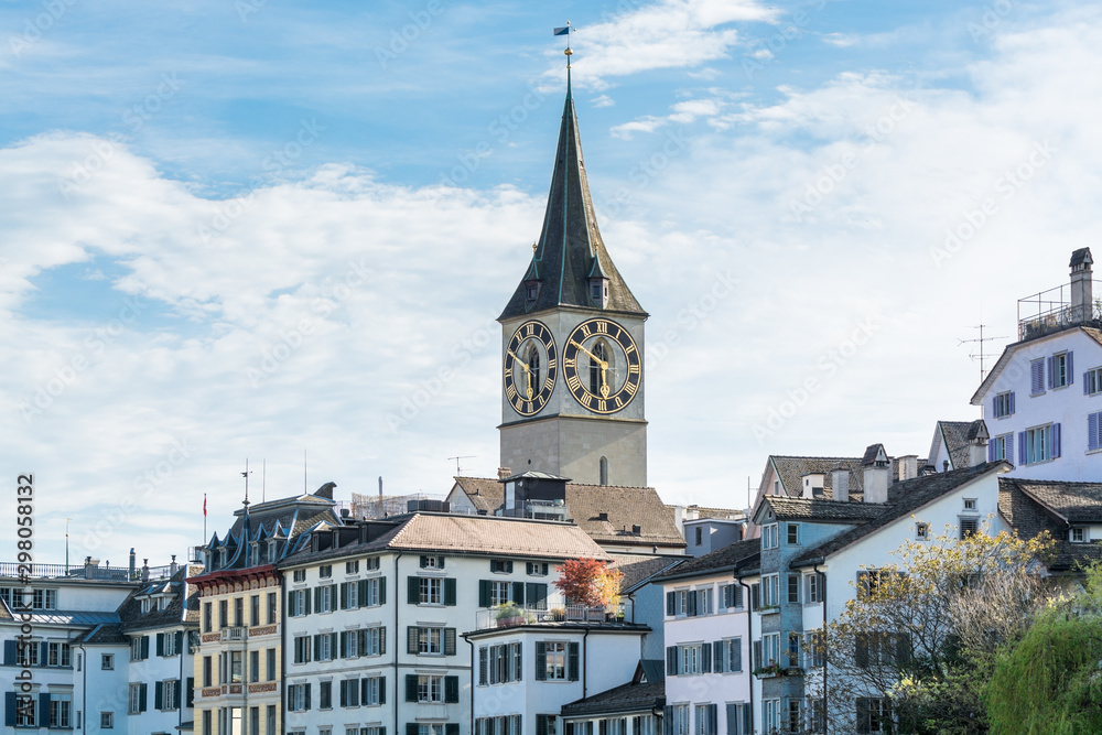 View of the historic center of Zurich at the bank of Limmat River, with beautiful house rooftops in spring, and St. Peter Pfarrhaus  Church clock tower
