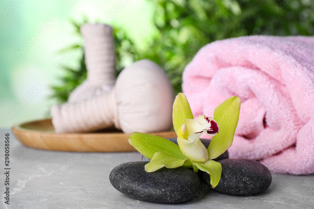 Spa stones, exotic flower, towel and herbal bags on grey marble table, space for text Spa stones, exotic flower, towel and herbal bags on grey marble table, space for text