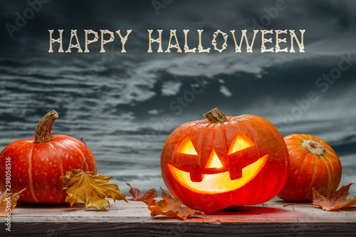 October luminous pumpkin, Jack-lantern, dry leaves against  gray evening sky. Background of wood. Happy Halloween.