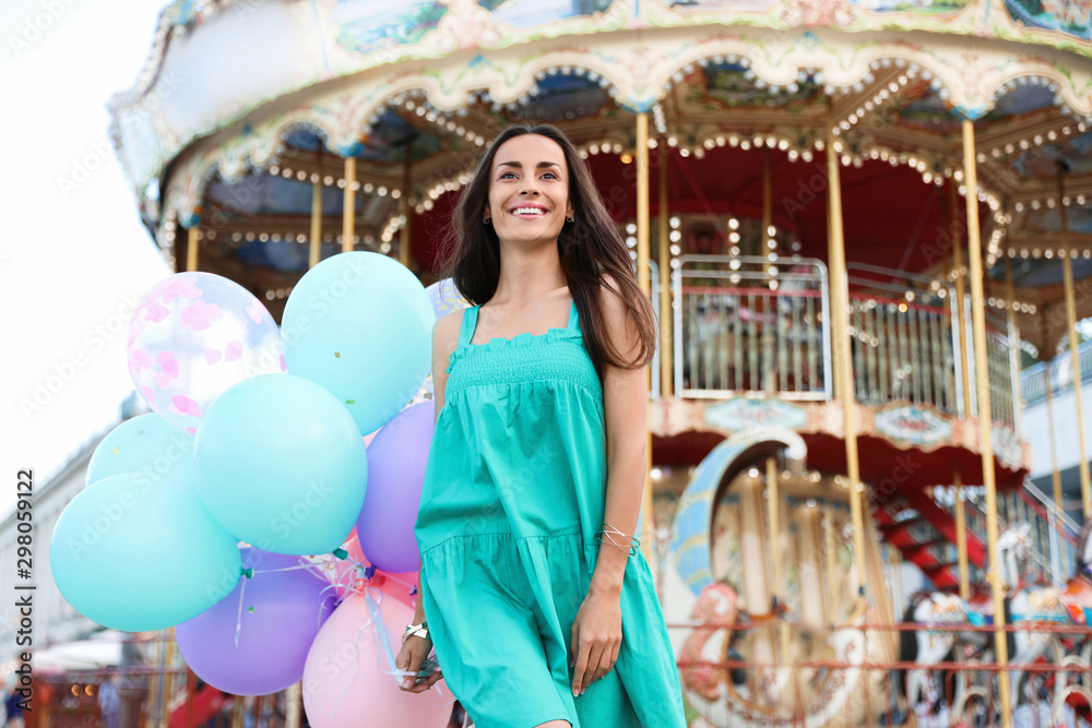 Attractive young woman with color balloons near carousel