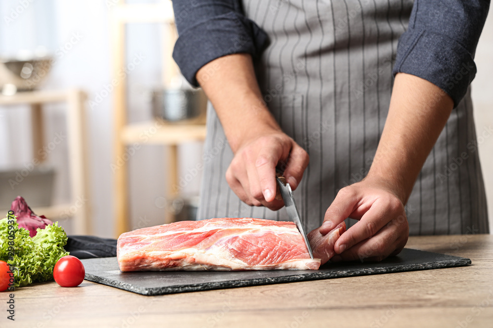 Man cutting fresh raw meat on wooden table in kitchen, closeup