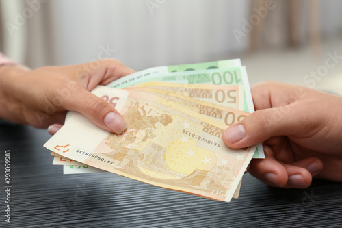 People with Euro banknotes at table indoors, closeup