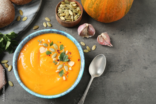 Delicious pumpkin soup in bowl on grey table, flat lay