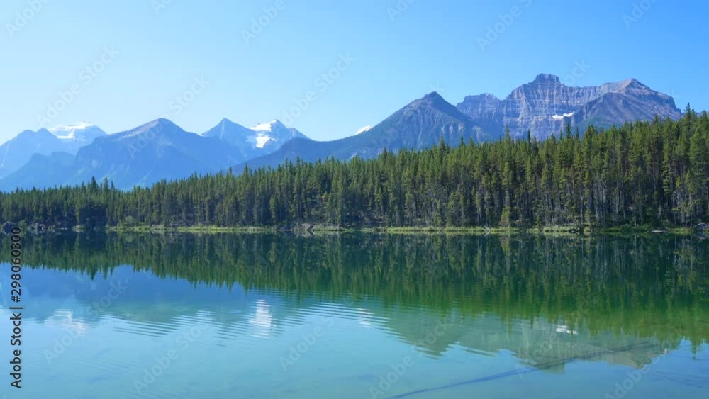 Natural landscape view of the local lake -herbert lake in banff alberta Canada in summer daytime with still claiming lake surface and mountain range with pine tree forest in background 