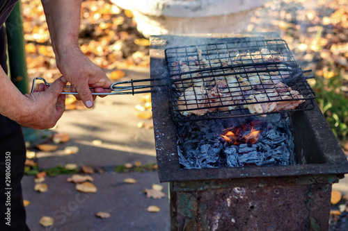 Men's hands cook barbecue from chicken on the grill on the street. Barbecue picnic in the country. Fire safety concept.