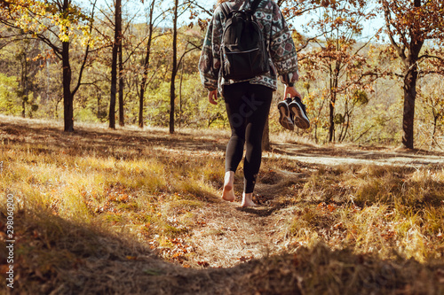 Beautiful young girl walking barefoot with sneakers in hand into the forest. There is a sunny autumn day with yellow leaves and dry grass. Photo with selective focus