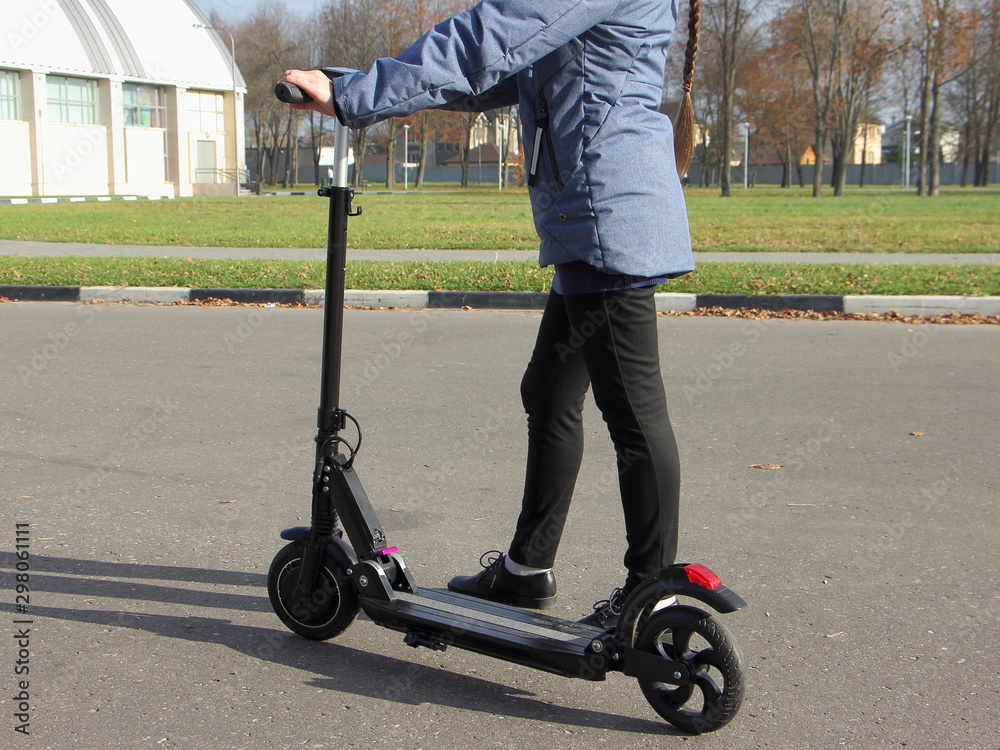 Obraz premium Dziewczyna w jesiennym ubraniu przyjeżdża z przenośną elektryczną hulajnogą na Park w słoneczny dzień, ekologiczny transport miejski