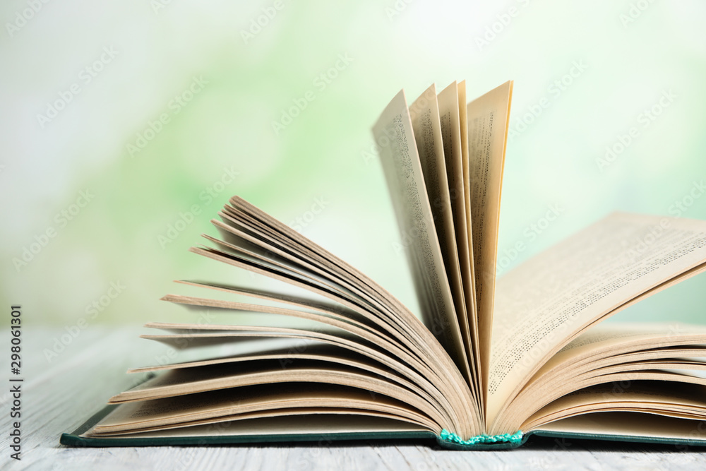 Open book on white wooden table against blurred green background, closeup Open book on white wooden table against blurred green background, closeup