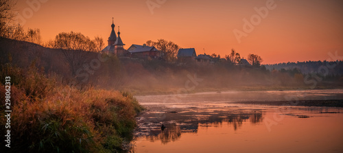Pink sunrise on the misty river with silhouette of the old church 