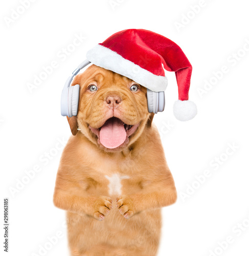 Happy puppy with santa hat listening wireless music with headphones. Isolated on white background © Ermolaev Alexandr