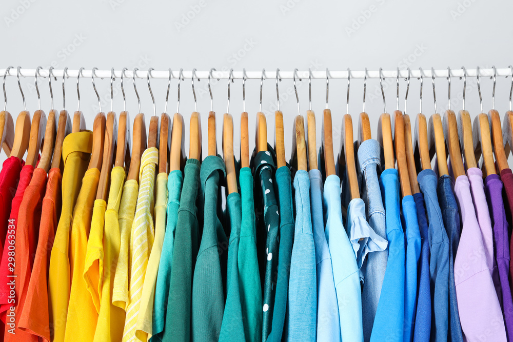 Rack with bright clothes on light blue background. Rainbow colors - obrazy, fototapety, plakaty 