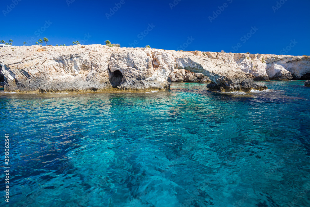 Rocky shore, clear turquoise water and blue sky.