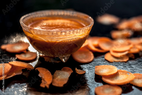 Carrot face mask on a black wooden surface consisting of some freshly sliced carrots paste, lemon juice, and honey well mixed in a glass bowl for the treatment of acne. photo