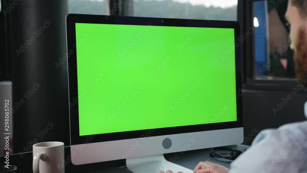 Modern computer greenscreen mock-up monitor close-up. Side view young business man working on personal computer keyboarding in corporate office space.