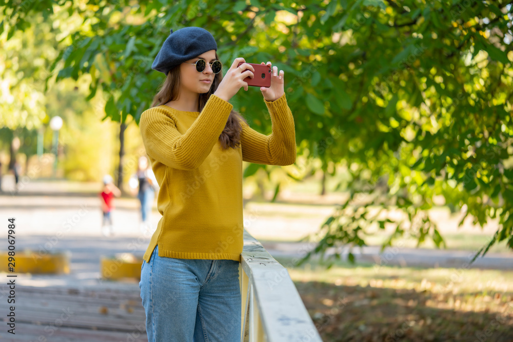 Young woman with a hat and sunglasses taking a photo outdoor in a park.