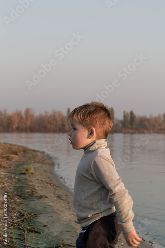Little kid boy plays near river, lake