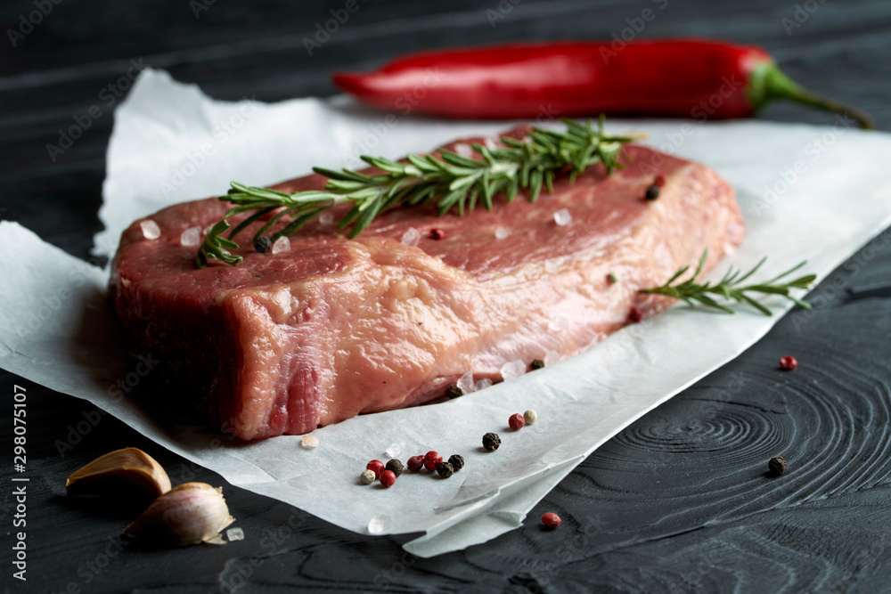 Raw fresh meat on paper with herbs, pepper and garlic on dark background Raw fresh meat on paper with herbs, pepper and garlic on dark background