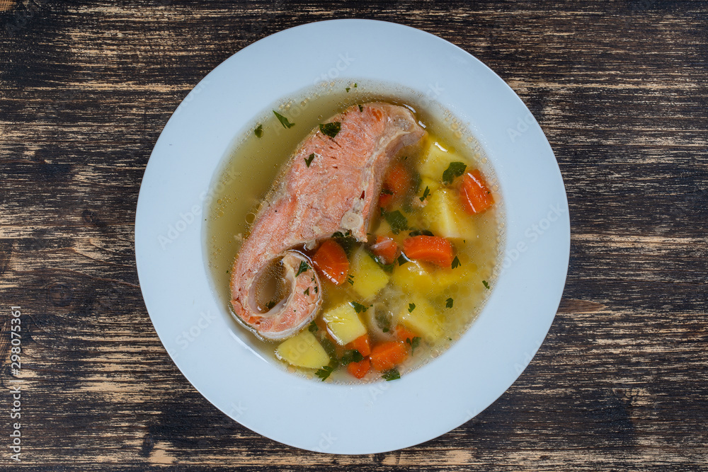 Fresh salmon fish soup with carrots and potatoes in a white plate, close up Fresh salmon fish soup with carrots and potatoes in a white plate, close up