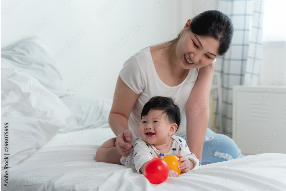 Young beautiful asian mother with asian baby on bed and playing toy ball together on white bed with feeling happy and cheerful and the baby that crawling on the bed.Baby family concept