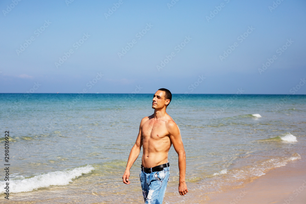 young muscular man resting and posing on the beach. A young man walks by the sea young muscular man resting and posing on the beach. A young man walks by the sea