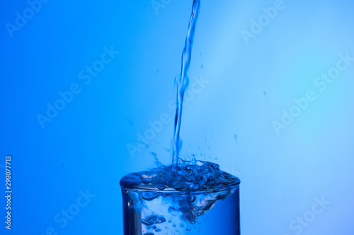 Chorro de agua llenando un vaso ya lleno y chapoteando y salpicando el agua que cae fuera del objeto de cristal