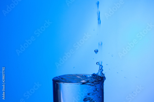 Chorro de agua llenando un vaso ya lleno y chapoteando y salpicando el agua que cae fuera del objeto de cristal