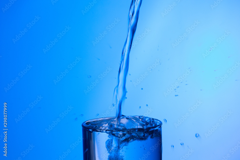 Chorro agua llenando y rebosando vaso de agua de cristal o plástico transparente sobre fondo azul foto de Stock | Adobe Stock