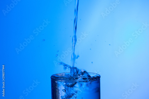 Chorro de agua llenando un vaso ya lleno y chapoteando y salpicando el agua que cae fuera del objeto de cristal