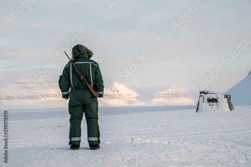 Man with a rifle looks out on the horizon in arctic landscape at Svalbard