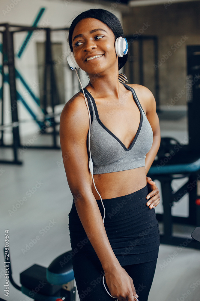 Beautiful black girl in the gym. A woman in a gray top. Lady with a headphones Beautiful black girl in the gym. A woman in a gray top. Lady with a headphones