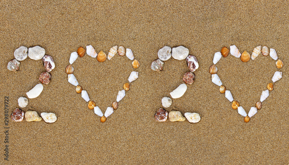 Pebble New Year 2020 number with shell heart shape on wet sandy beach. Summer 2020 holidays concept. 