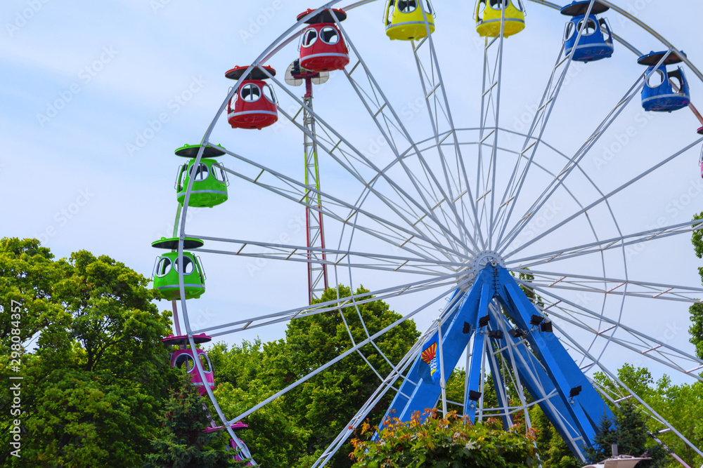 Ferris wheel without people , among green on the blue sky background